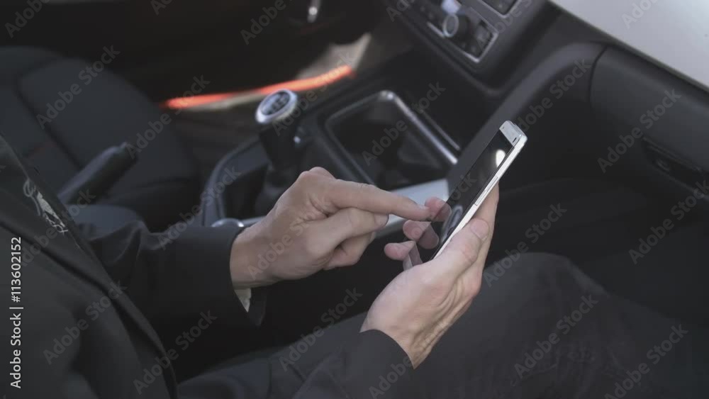 Caucasian man typing a sms on a smartphone in the passenger seat in a car. For concepts such as sms, text messaging, chat and web browsing. Caucasian man typing a sms on a smartphone in the passenger seat in a car. For concepts such as sms, text messaging, chat and web browsing.