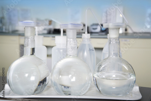 Group of laboratory flasks with a clear liquid on desk in laboratory interior. © katrin_timoff