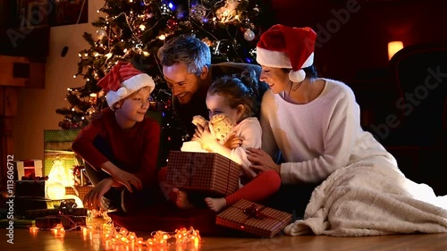 a family near the Christmas tree, the girl finds a teddy bear in her gift box
