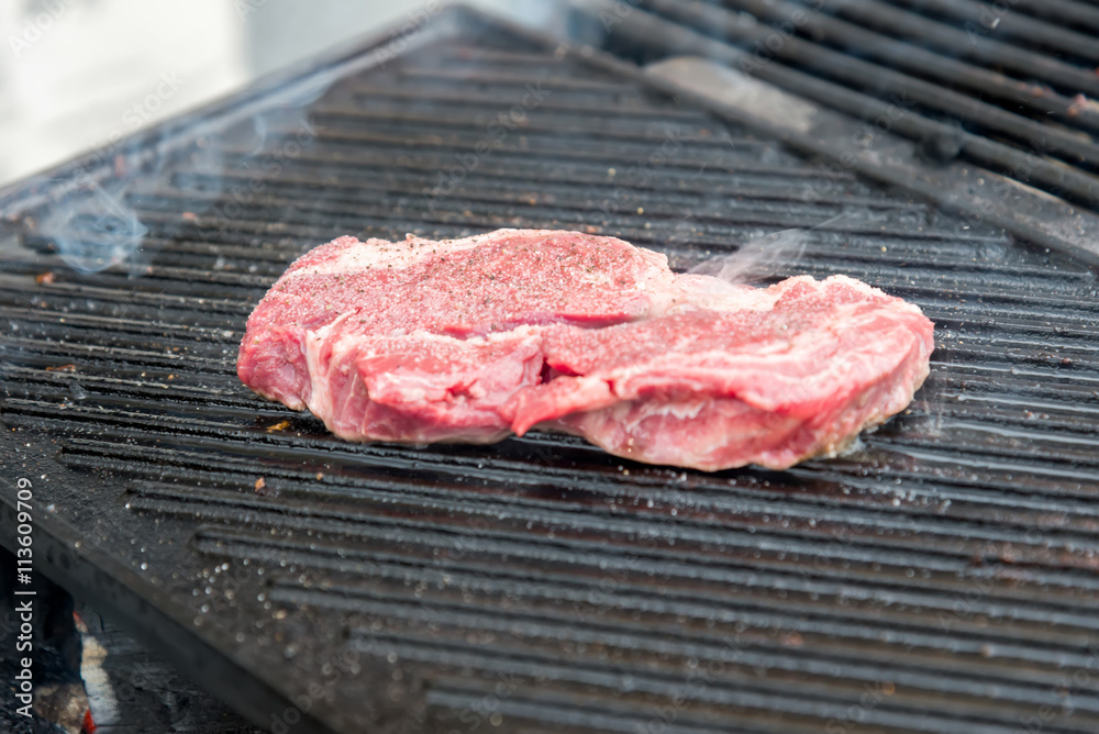 raw steak with spices on metal grill