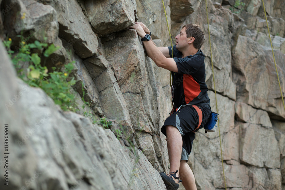 Male rock climber clings to a cliff