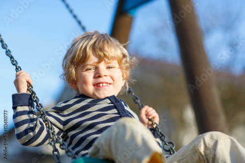 Adorable toddler boy having fun chain swing on outdoor playground