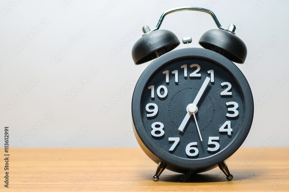 Black alarm clock place on wood table in burred background Black alarm clock place on wood table in burred background