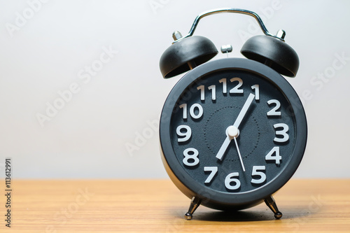 Black alarm clock place on wood table in burred background