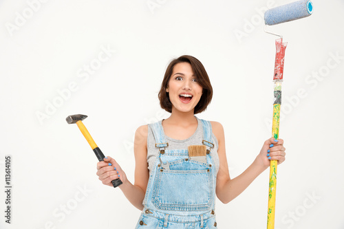 Portrait of surprised girl, holding hammer and painting roller