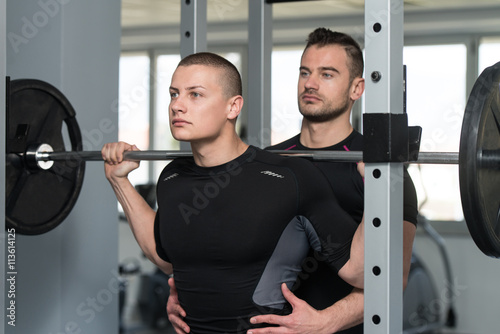 Woman With Personal Trainer At Barbell Squat