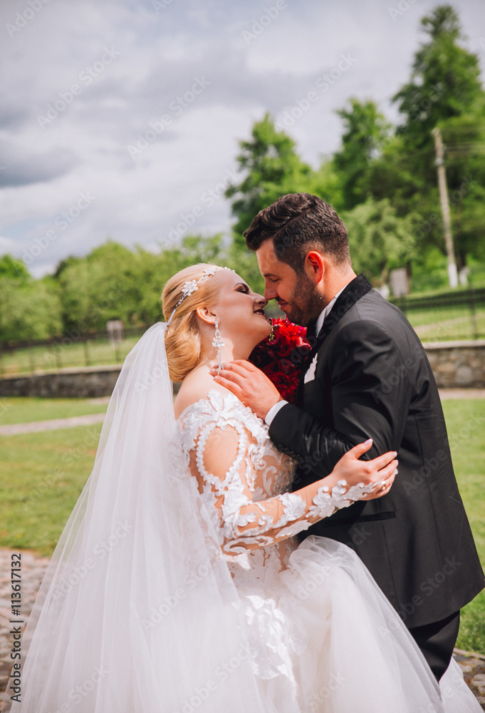 Naklejka premium Bride and groom at wedding Day walking Outdoors on spring nature. Bridal couple, Happy Newlywed woman and man embracing in green park. Loving wedding couple outdoor. Bride and groom