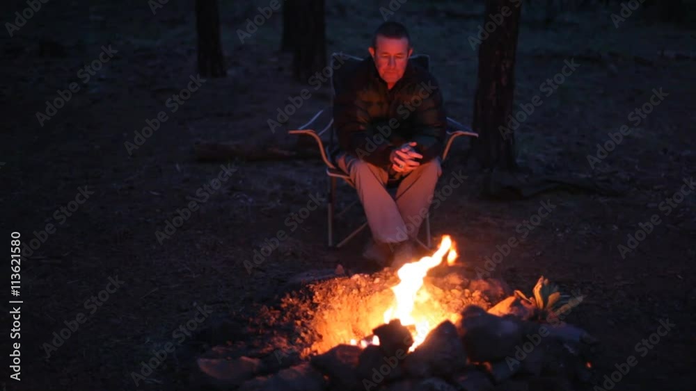 A man sitting by a camp fire in deep thought