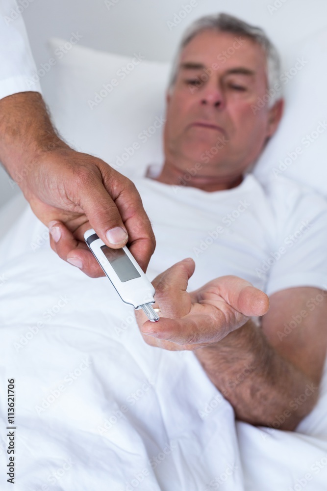 Male doctor testing diabetes of senior man on glucose meter Male doctor testing diabetes of senior man on glucose meter