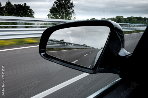 Specchietto retrovisore laterale di una macchina che viaggia in autostrada © vpardi