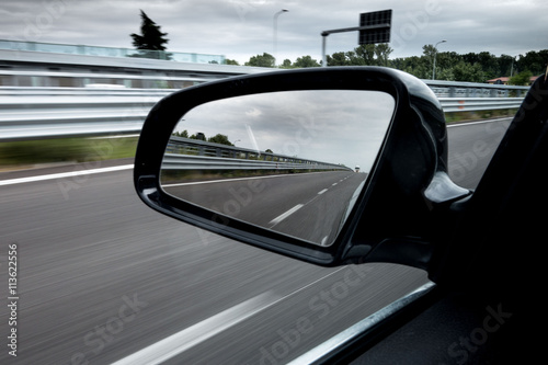 Specchietto retrovisore laterale di una macchina che viaggia in autostrada photo