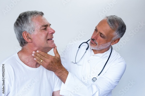 Male doctor examining senior mans neck