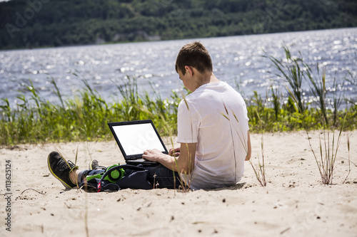 teenager working at a laptop on the beach