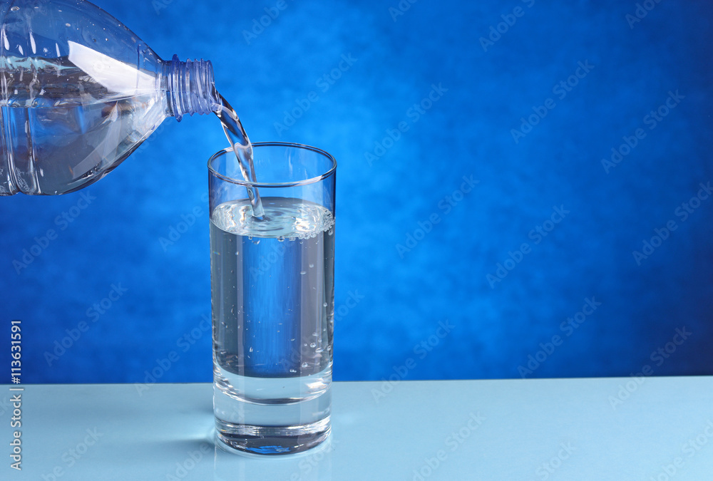 L'acqua fredda fluisce dal biberon al bicchiere. Versare l'acqua da una  bottiglia in un bicchiere su sfondo blu. Posiziona per testo Foto stock -  Alamy
