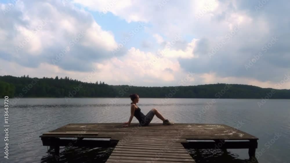 Young woman sits on a wooden pier on the lake Young woman sits on a wooden pier on the lake