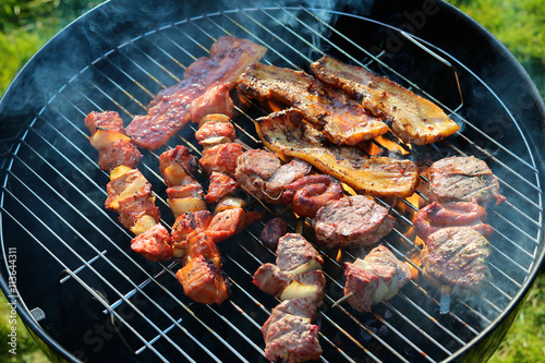 Assorted mixed grill on wooden skewers from chicken meat, lamb and pork, marinated spareribs, sausages and various vegetables roasting on barbecue grid cooked for summer family dinner