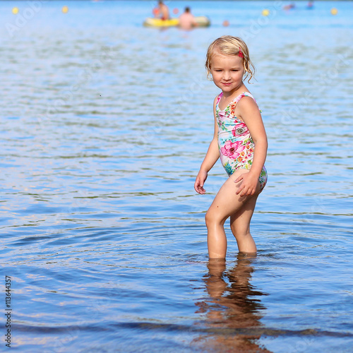 Happy kid playing in the lake. Healthy smiling toddler girl enjoying summer vacation outdoors.