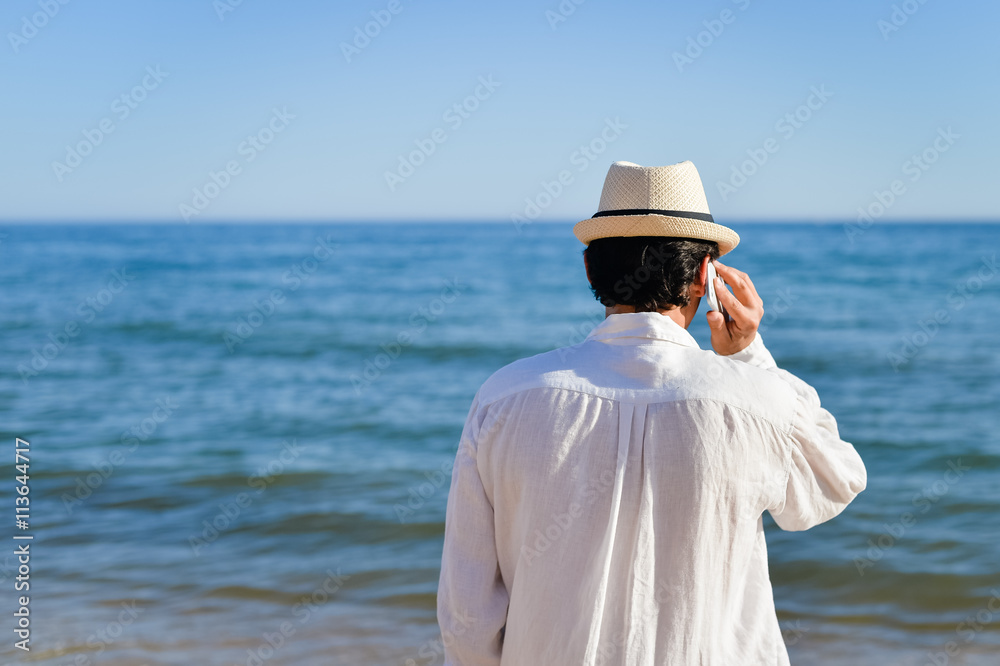 Back view of man talking holding mobile phone, blue sky sea outdoors background