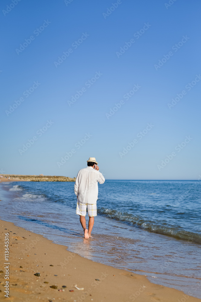 Young stylish man on the phone walking on beach