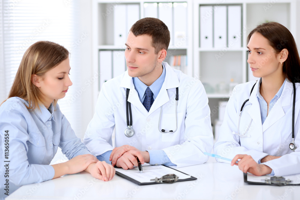 Two doctors and patient sitting at the table in medical cabinet. High level and quality medical service concept. Two doctors and patient sitting at the table in medical cabinet. High level and quality medical service concept.