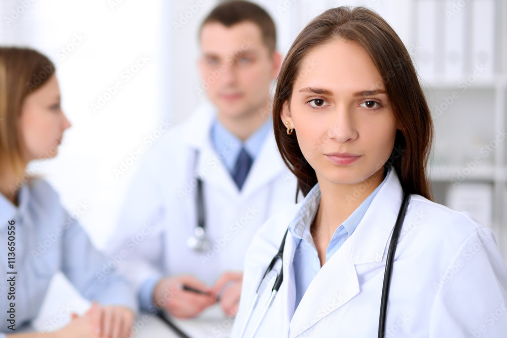 Young beautiful female doctor smiling on the background with patient and his doctor in hospital. High level and quality medical service concept. Young beautiful female doctor smiling on the background with patient and his doctor in hospital. High level and quality medical service concept.