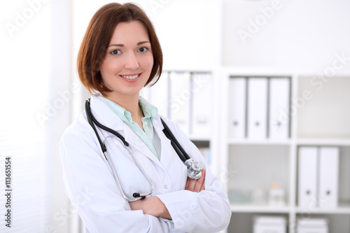 Young brunette female doctor standing with arms crossed and smiling at hospital. Health care, insurance and help concept. Physician ready to examine patient