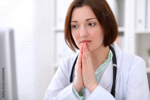 Young brunette female doctor sitting at the table and working at hospital office.  Doctor is in trouble with diagnosis. Health care, insurance and help concept.