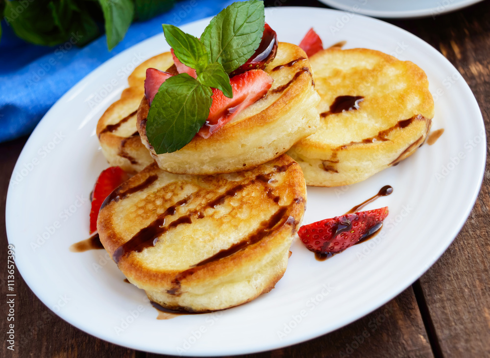 Rustic pancakes with fresh strawberries and chocolate on a white plate