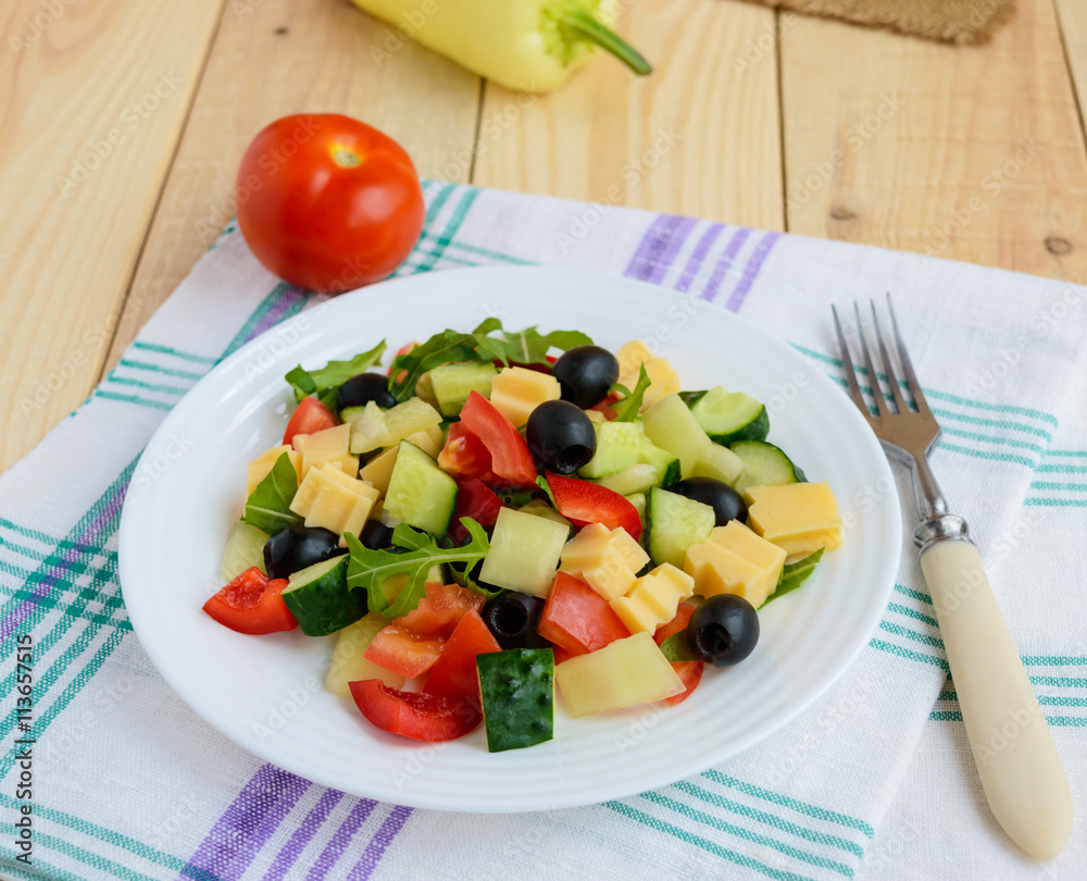Fresh diet salad with cucumbers, tomatoes, olives cheese, bell peppers, arugula on a light wooden background