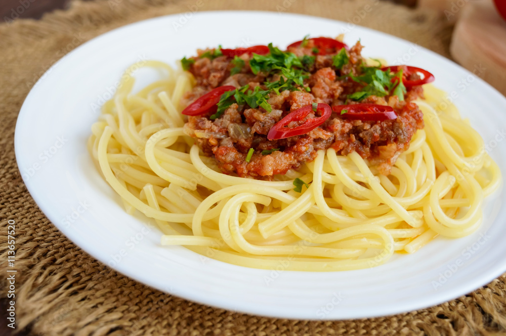 Spaghetti Bolognese with chili on a white plate on a wooden background. Close up