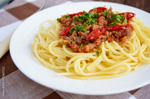 Spaghetti Bolognese with chili on a white plate on a wooden background. Close up