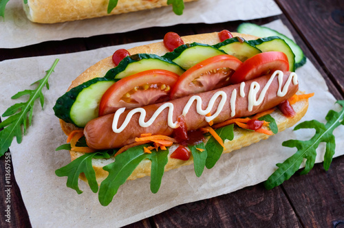 Home made hot dogs with vegetables, juicy sausage and arugula on the wooden background. Close-up.