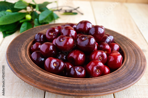 Ripe black cherries in a clay bowl on a light wooden background. Close-up.