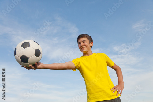 Happy teenager holds a soccer ball in his hands, on a background © olezzo