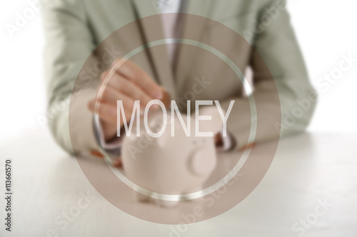 Money icon. Man putting coin into piggy bank at wooden table closeup