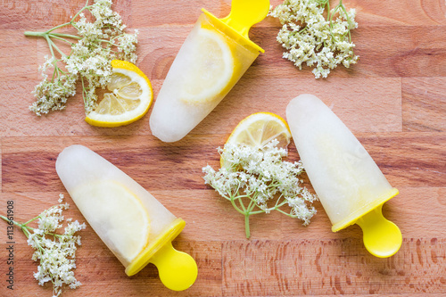 Elderberry ice lollies with lemon and flowers with flat lay photography. Horizontal image of fresh icecream with natural ingredients like berries and lemond with wooden table background.