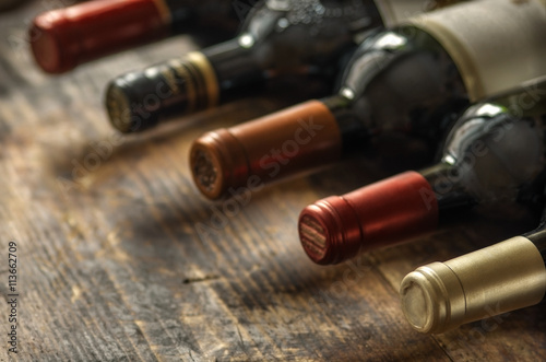 Row of wine bottles with dry red  wine on wooden background. Low depth of field. Wine making and wine shop concept.