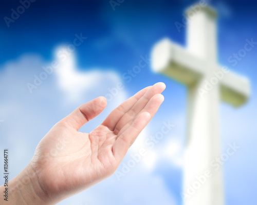 hand praying over blurred the cross on the sky background.