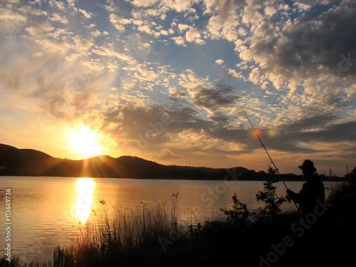 Fisherman standing on a shore with background sun rays