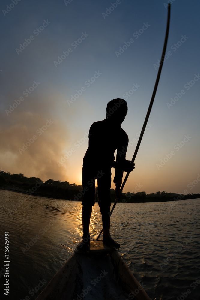 boy pushing a canoe with a long wooden pole in the sunset