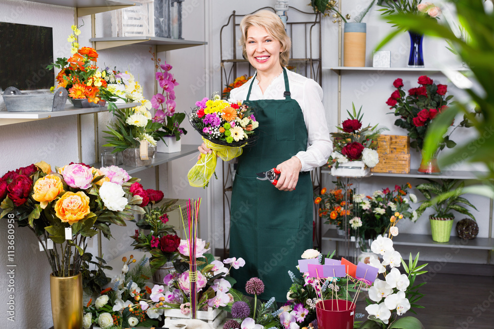 Female florist wearing an apron and happily preparing flowers