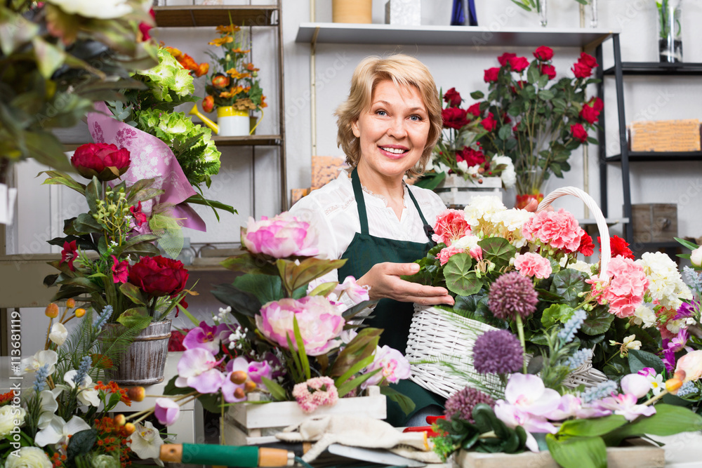 Female florist wearing an apron and happily standing among flowe