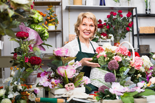 Female florist wearing an apron and happily standing among flowe