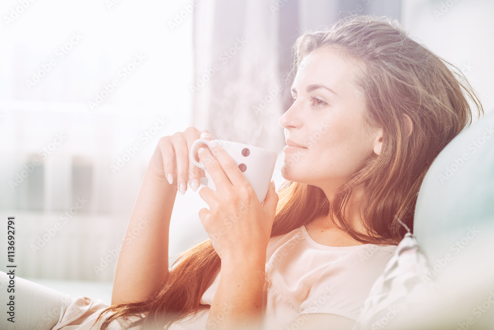 Young woman sitting on couch at home and drinking coffee. Casual