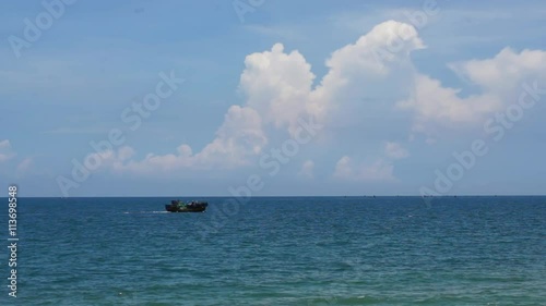 Small fishing boat crossing the blue ocean under the bright blue sky.