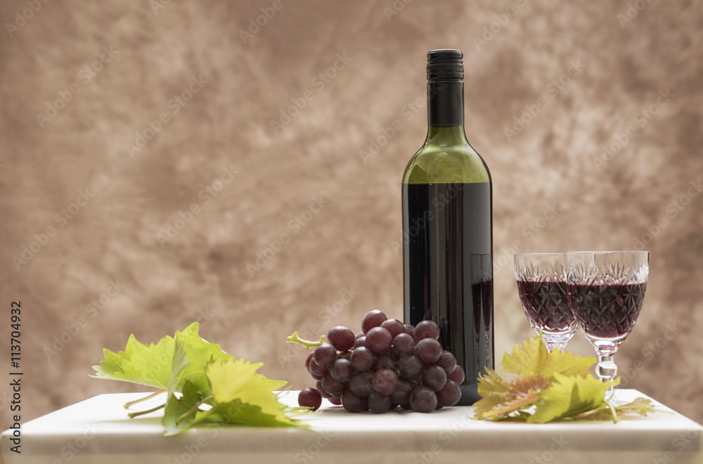 Background image of a red wine bottle with two glasses, red grapes and vine leaves. Taken with copy space.