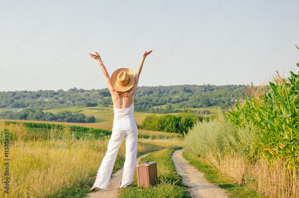 Fototapeta premium Elegant lady holding suitcase, countryside road outside background