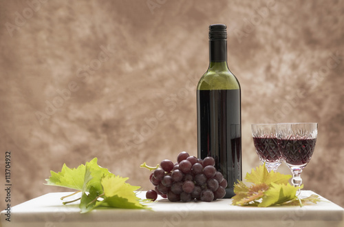 Background image of a red wine bottle with two glasses, red grapes and vine leaves. Taken with copy space.