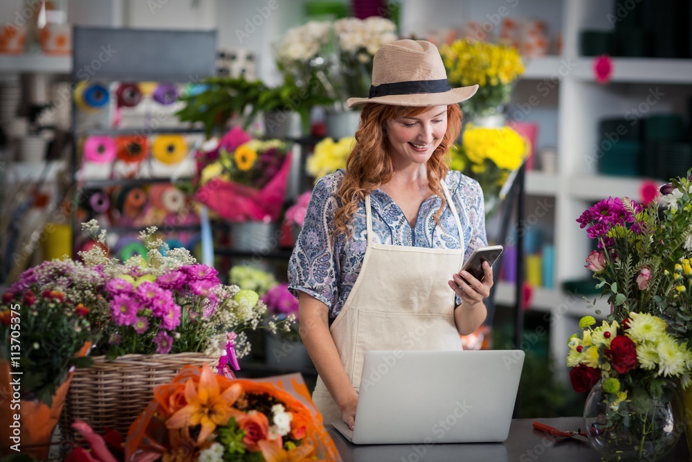 Female florist using mobile phone while using laptop