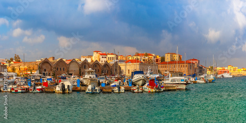 Panorama of Chania Arsenals, the Venetian shipyards, and fishing boats in old harbour of Chania with Lighthouse in sunny and cloudy summer morning, Crete, Greece